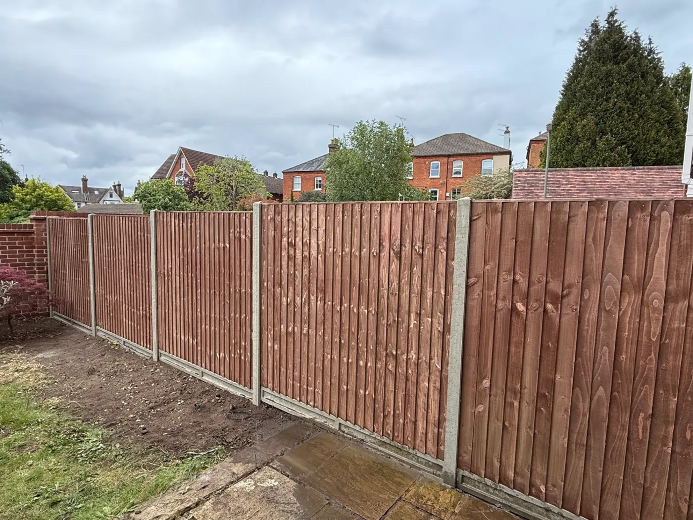 Brown stained featheredge fencing with concrete posts behind a house