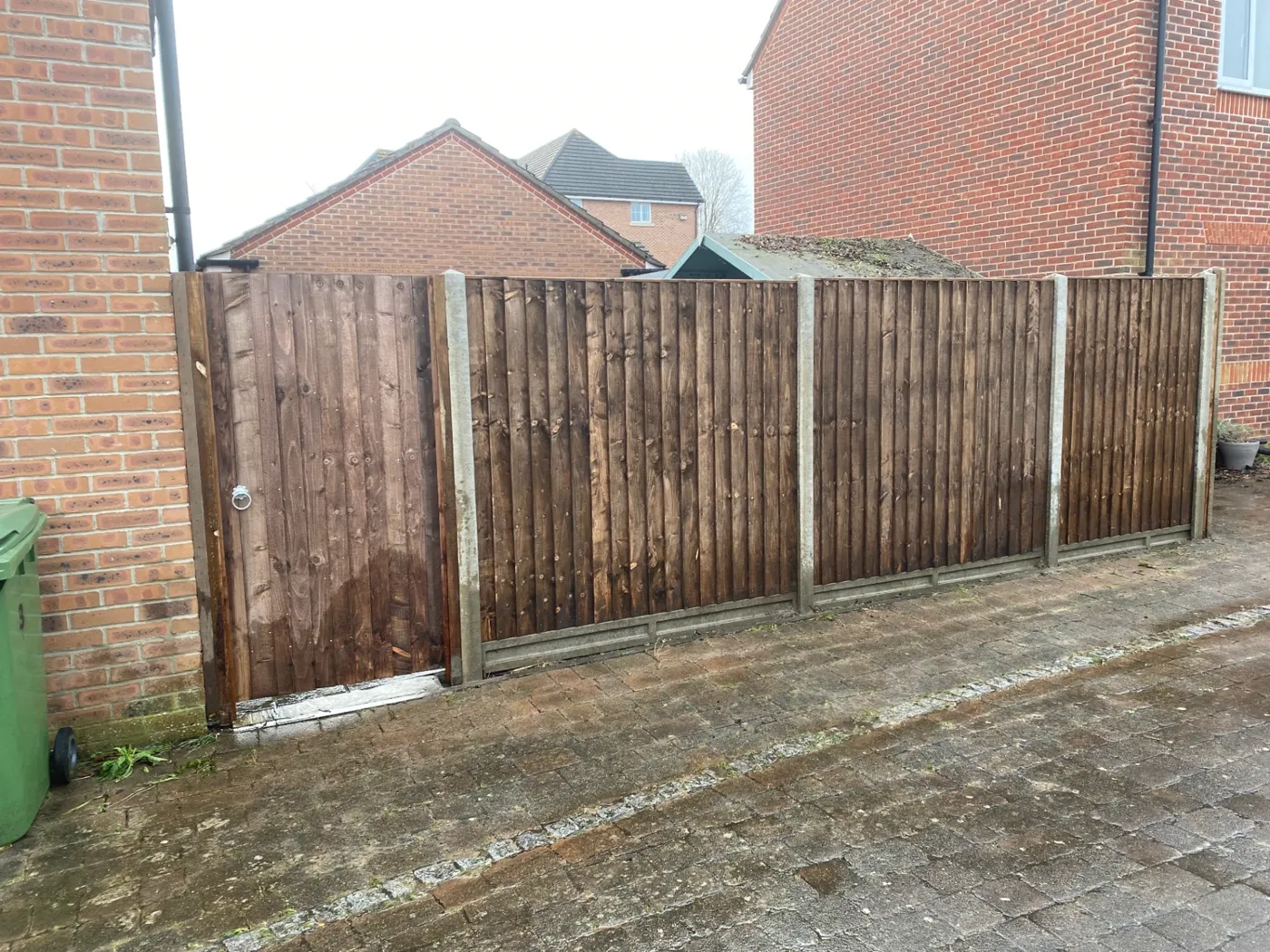 Fence panels and matching side gate installed on a paved driveway